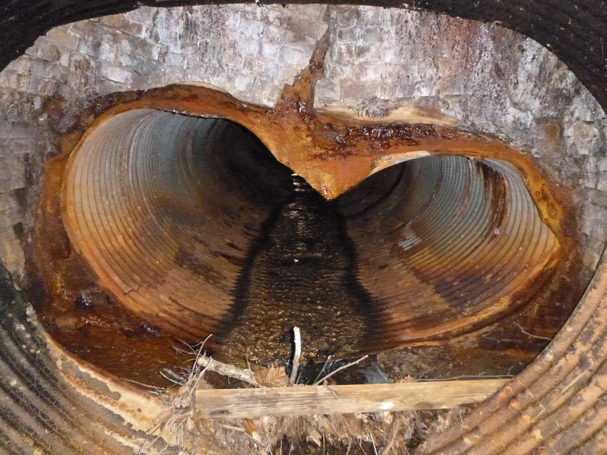 A culvert interior. The culvert is rusting and buckling.