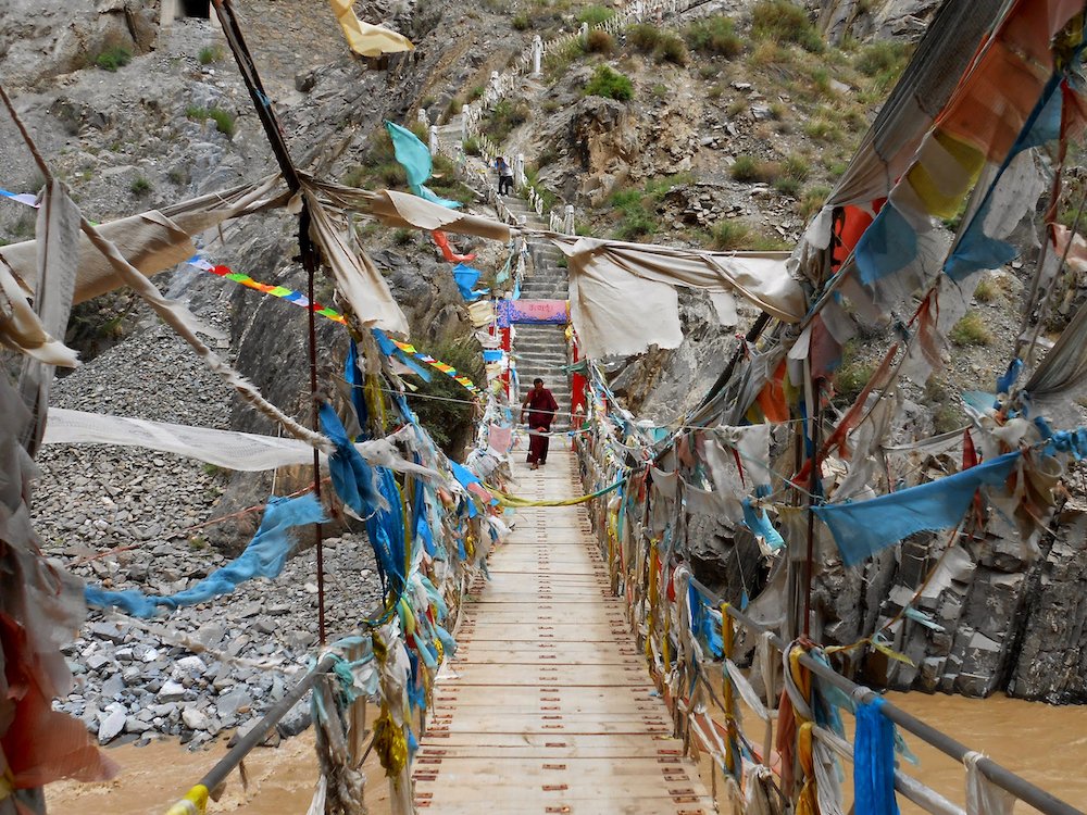  A Tibetan monk crosses a swinging bridge covered in prayer flags. 