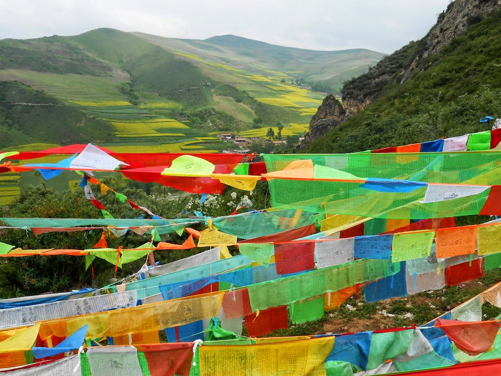  Prayer flags flutter against a mountain backdrop at Gönlung Jampa Ling monastery. 