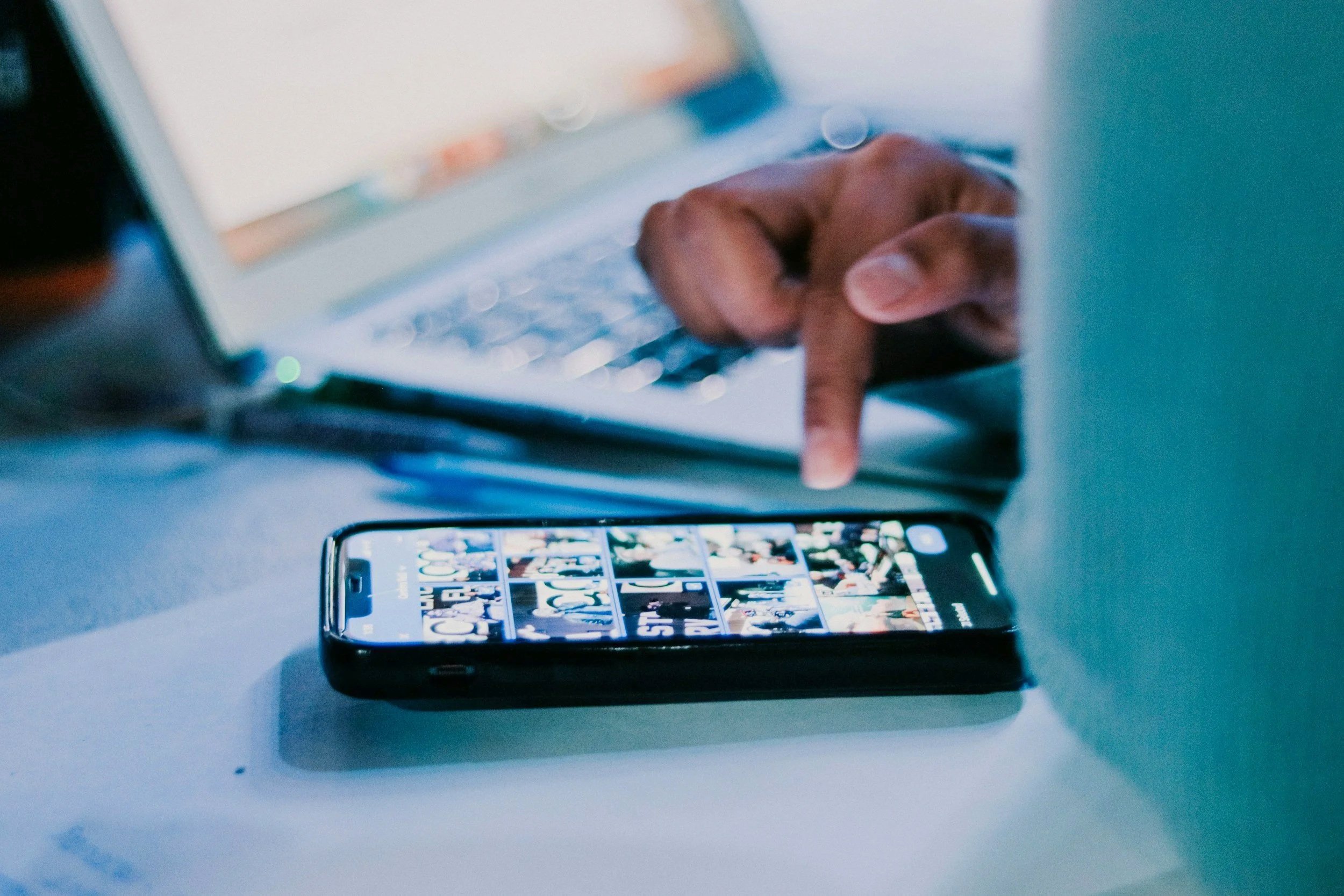 Close-up of a hand with a finger pointing at a smartphone screen displaying a grid of images on Instagram.