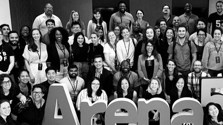 Group of diverse people gathered for a group photo at an event, with a large sign spelling 'Arena' in front.