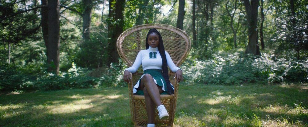 Selah Summers in a Haldwell cheer leading uniform sat on a wooden chair in a forest. Captured by Jomo Fray