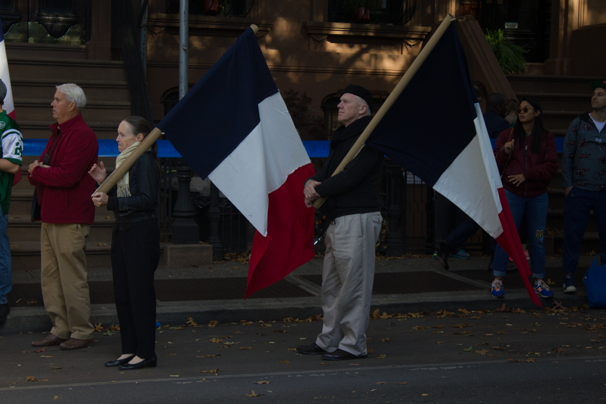 Two people with French flags stand ready to cheer on cyclists and runners in Brooklyn.