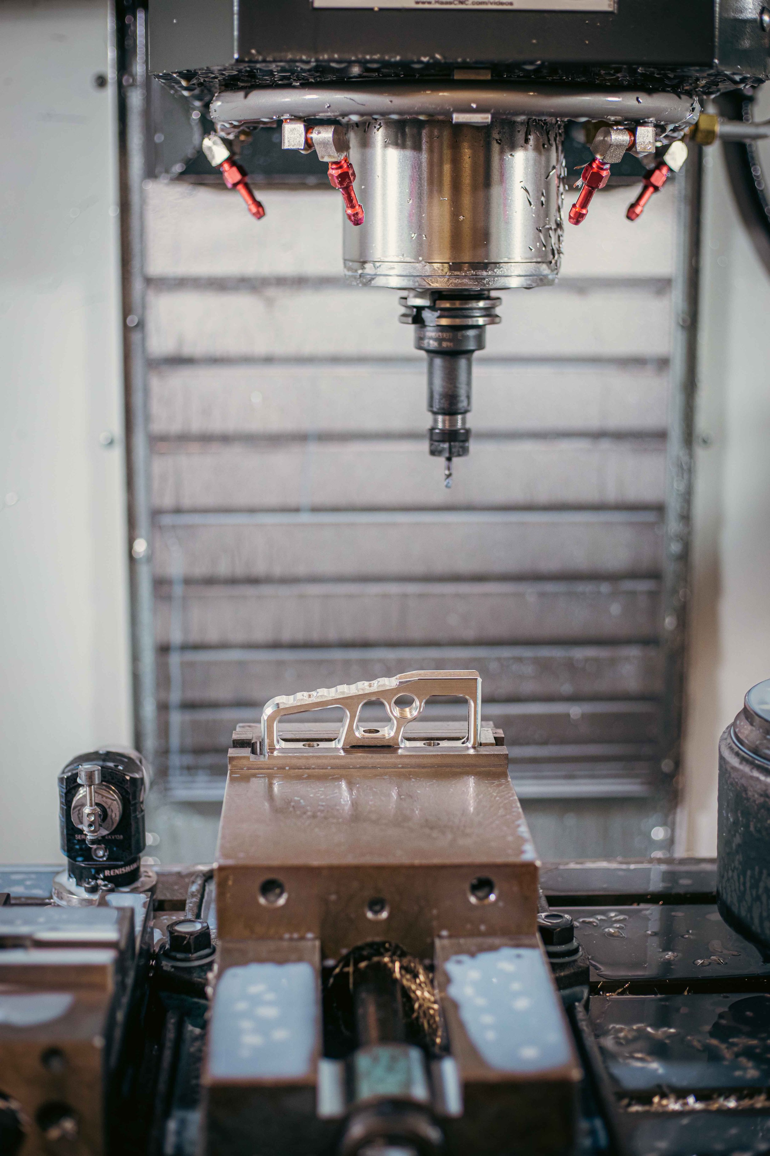 CNC machine milling a metallic piece, with cutting tool and coolant nozzles visible.