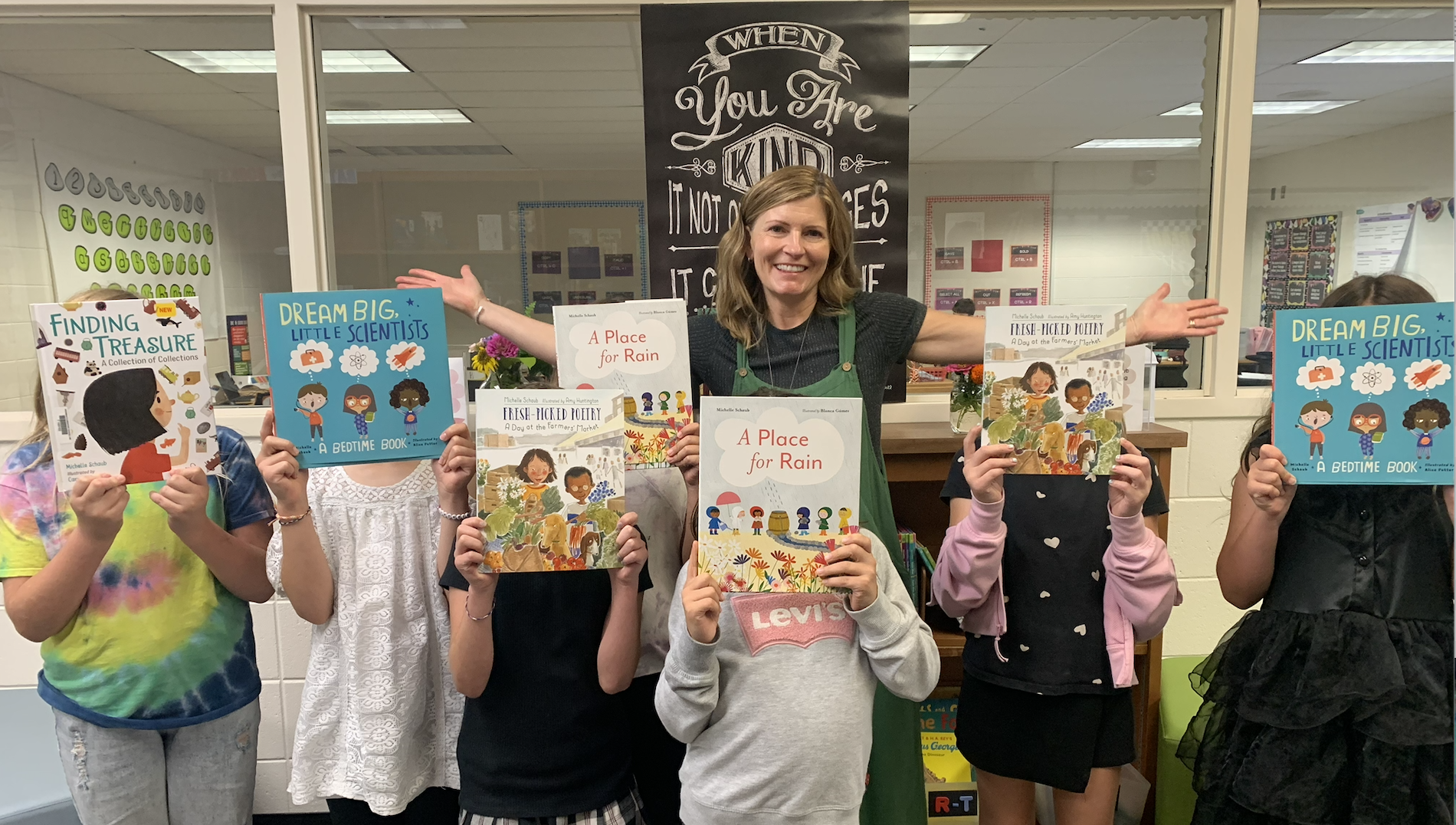 Children's author Michelle Schaub posing with a group of students holding up her books during an author visit to an elementary school.