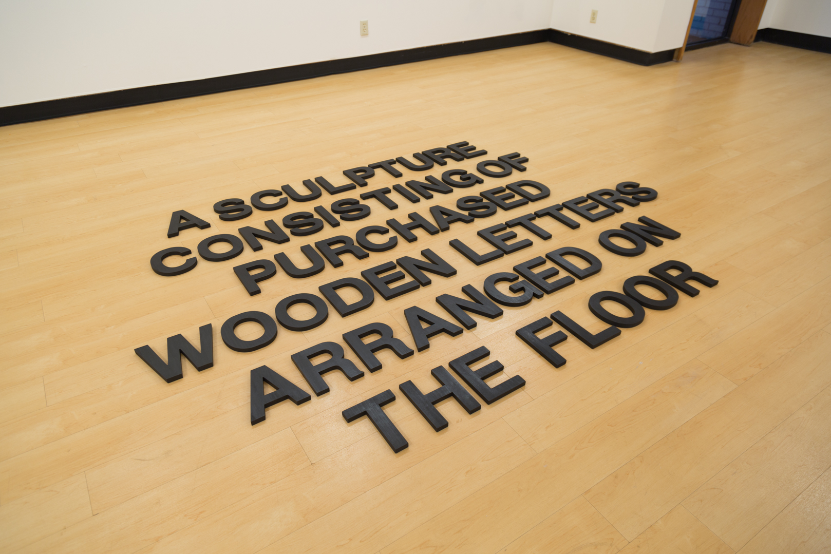    A Sculpture Consisting of Purchased Wooden Letters Arranged on the Floor , 2019  Wood, India ink, and wax Size variable 