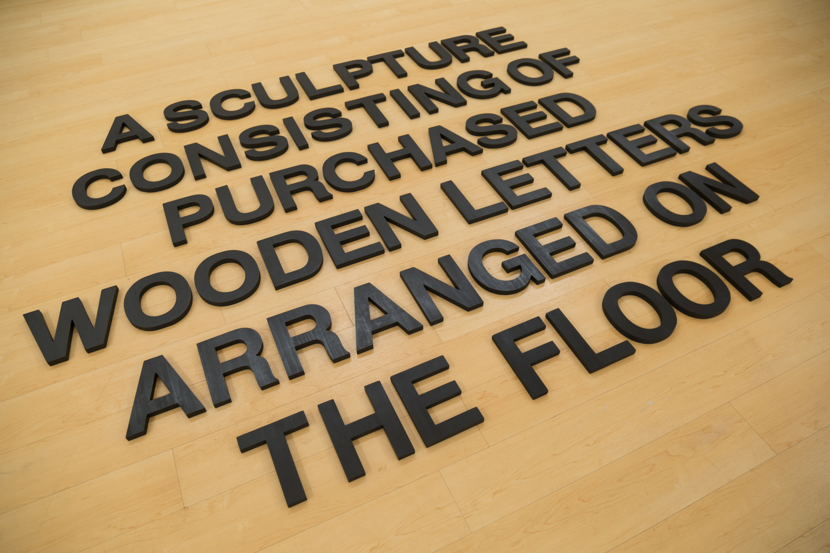 A Sculpture Consisting of Purchased Wooden Letters Arranged on the Floor , 2019 Wood, India ink, and wax Size variable