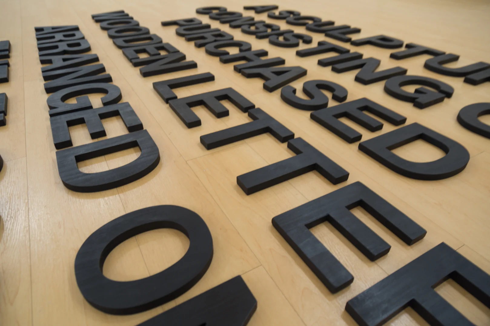 A Sculpture Consisting of Purchased Wooden Letters Arranged on the Floor , 2019 Wood, India ink, and wax Size variable