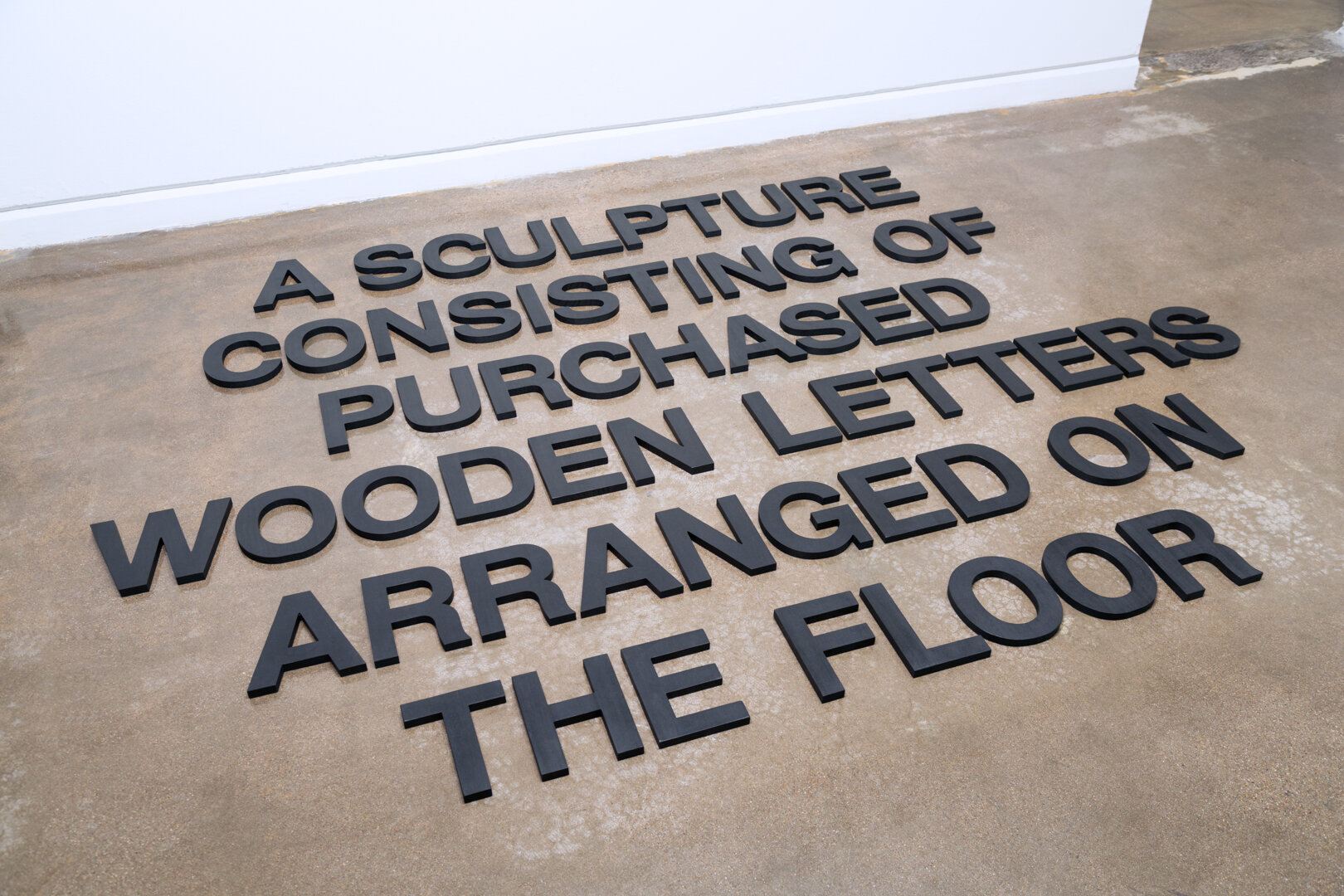    A Sculpture Consisting of Purchased Wooden Letters Arranged on the Floor , 2019  Wood, India ink, and wax Size variable 