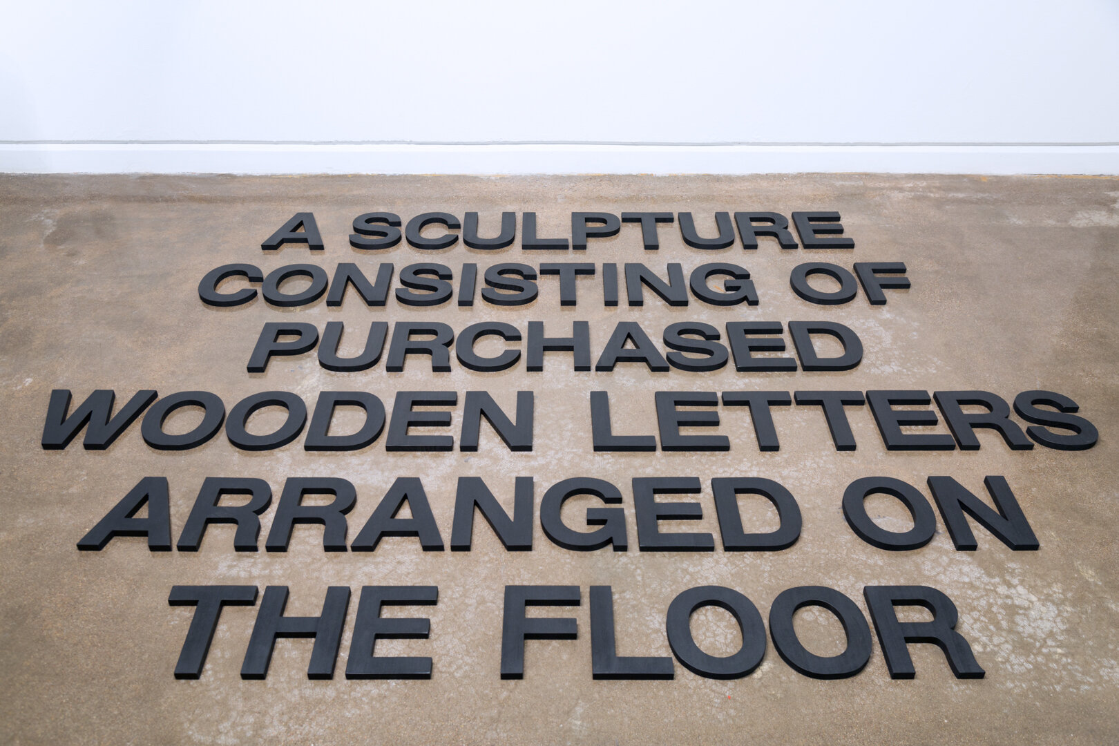    A Sculpture Consisting of Purchased Wooden Letters Arranged on the Floor , 2019  Wood, India ink, and wax Size variable 