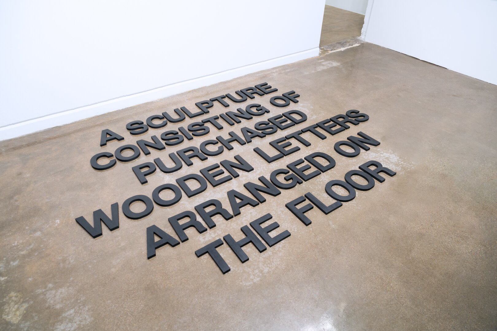    A Sculpture Consisting of Purchased Wooden Letters Arranged on the Floor , 2019  Wood, India ink, and wax Size variable 