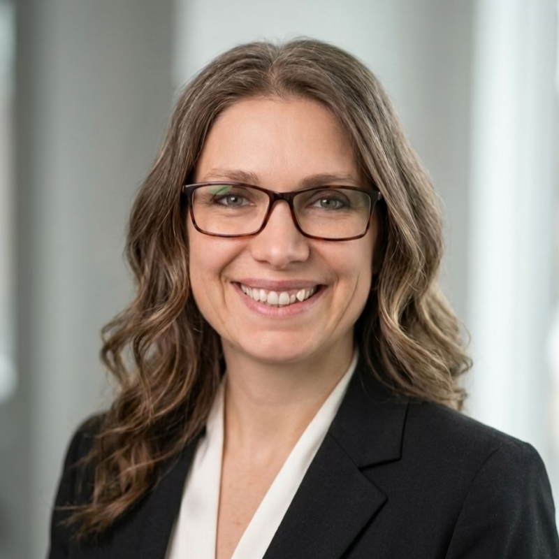 Professional woman with wavy brown hair and glasses smiling in an office setting.
