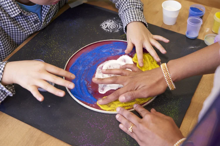 Grade 4 students using a stencil to create Rangoli with colored rice flour