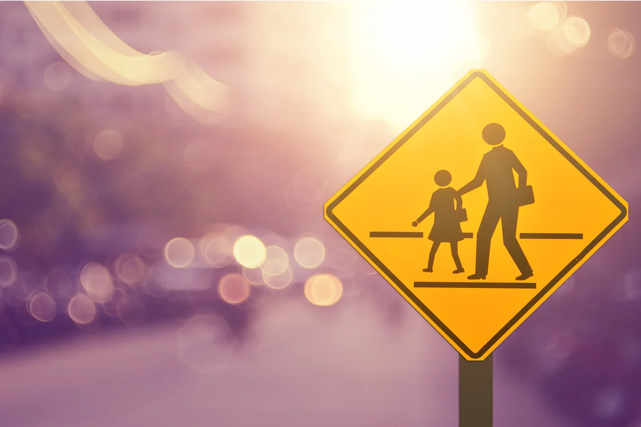 A yellow school crossing sign with blurred road background