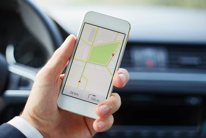A man's hand holding a mobile phone showing a map application in a car