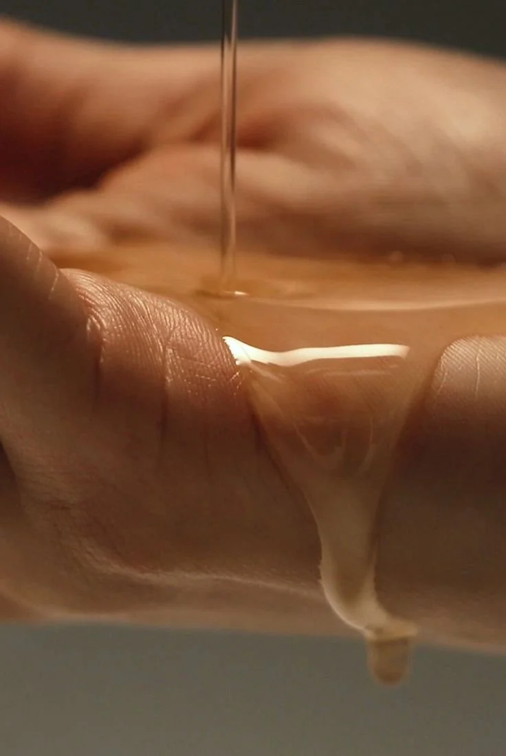 Close-up of a hand holding a glass with a brown liquid, with liquid pouring into the glass.