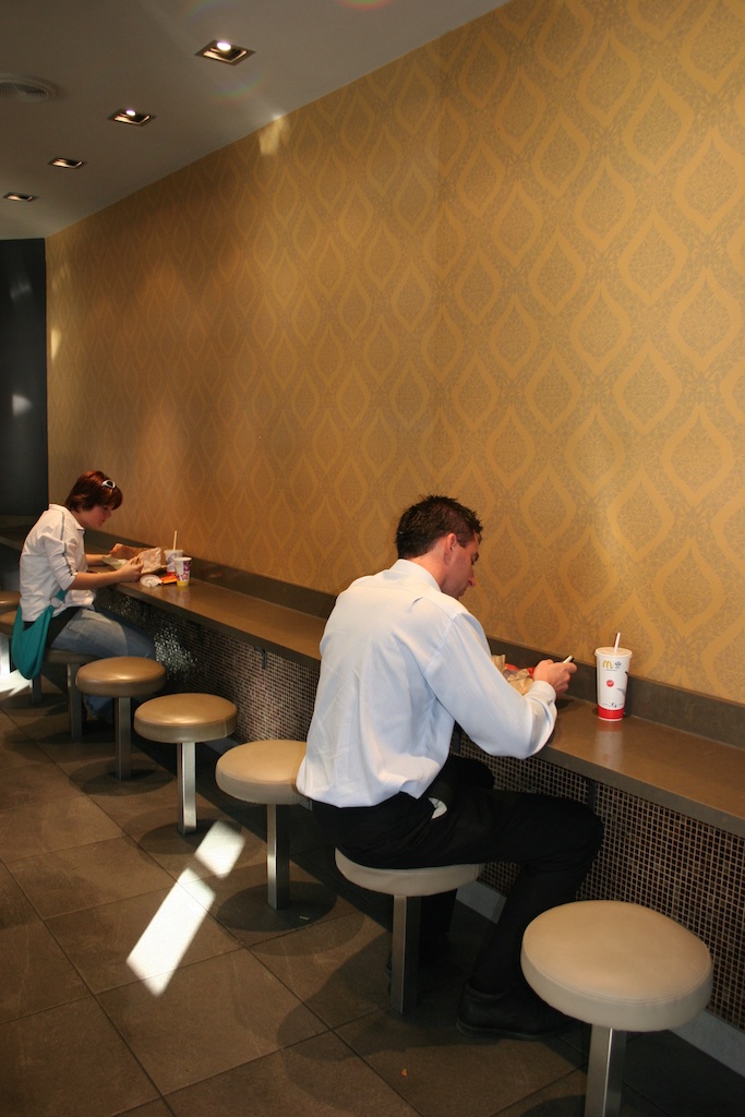 Sharing a long-distance meal facing a wall. McDonalds, Sydney, Australia.