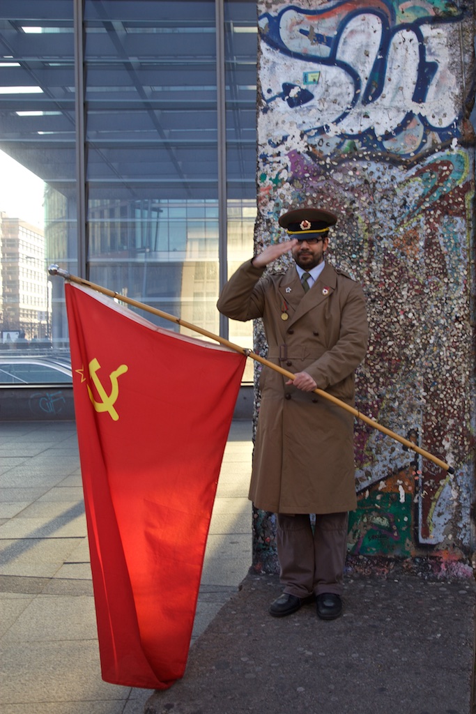 A survivor of the defunct Soviet Union standing by a remnant of the Berlin cold war wall. Berlin, Germany.