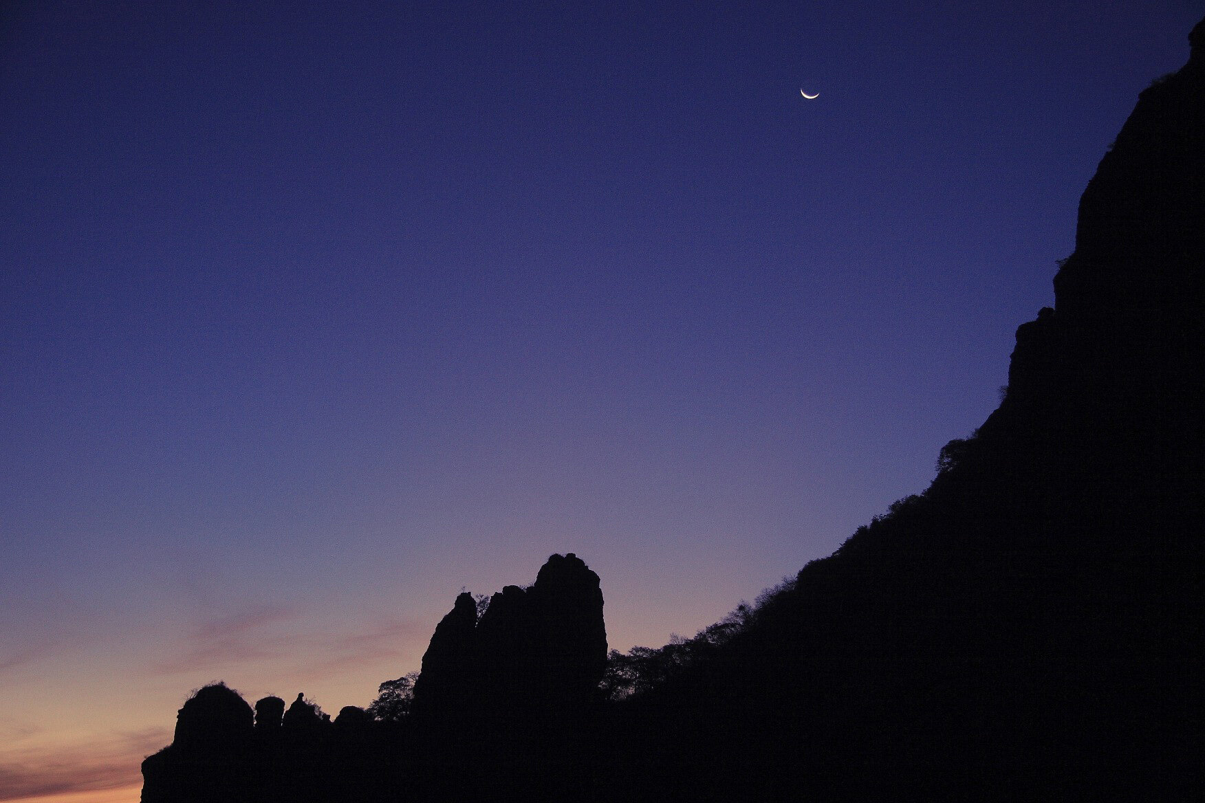 A tired moon over crumbling mountains.