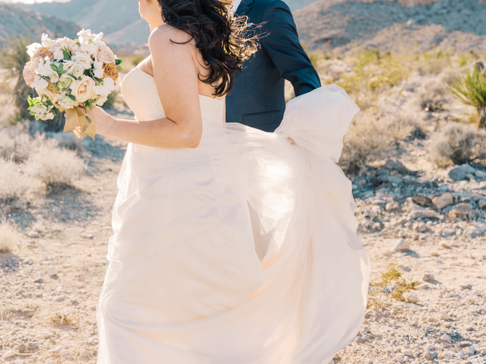groom holding onto brides dress as their walking through the desert