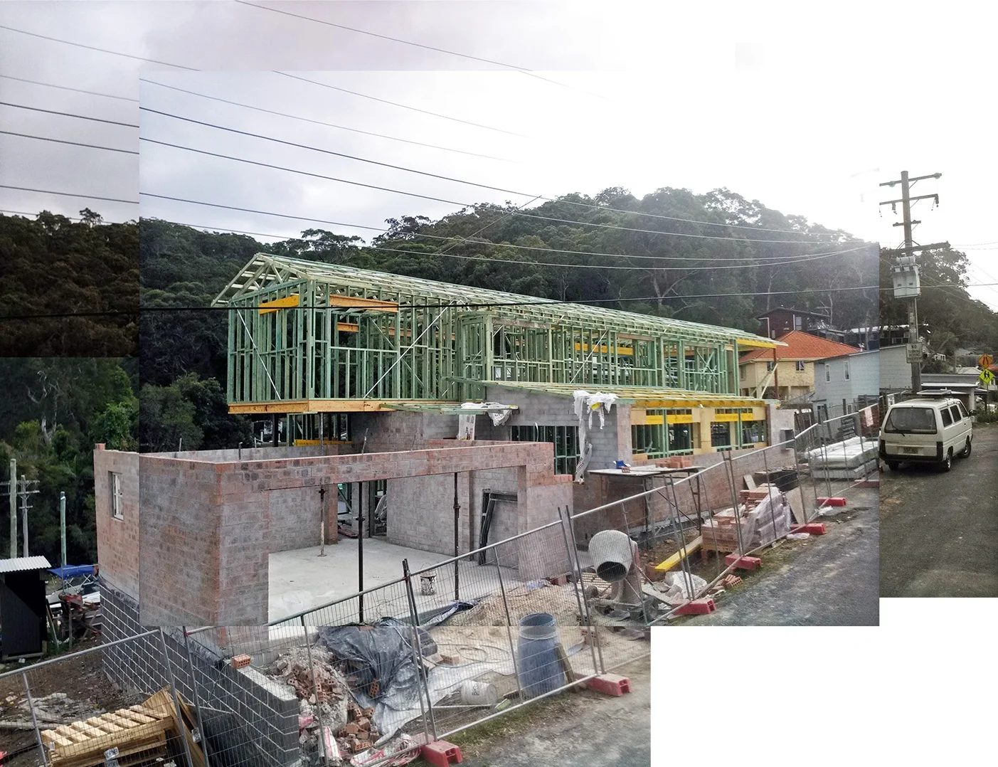 Construction site with a partially built two-story house, green framing, brick walls, construction materials, and equipment, with a hillside and trees in the background.