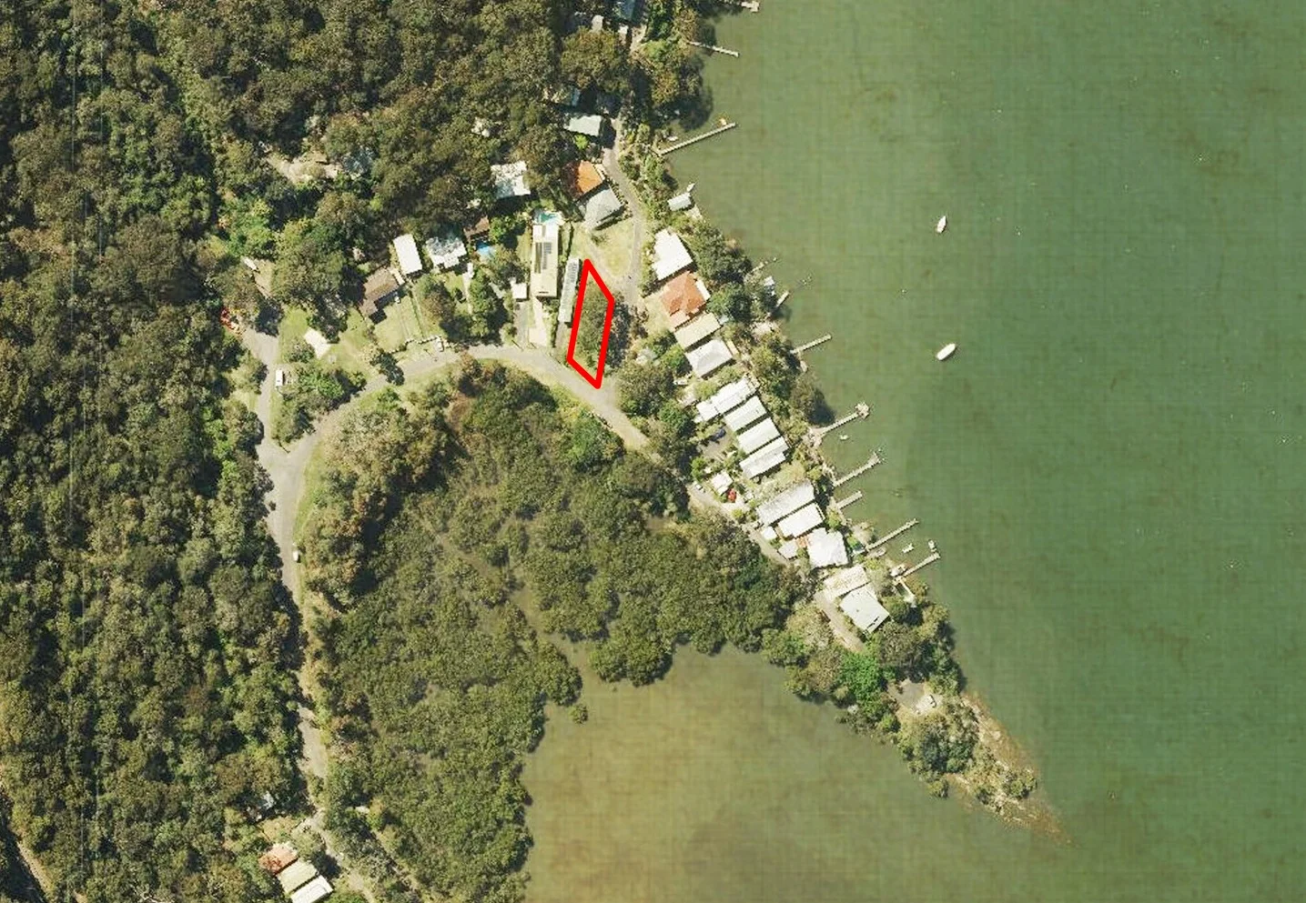 Aerial view of a lakeside neighborhood with houses, trees, and dock structures along the waterfront. A red outline highlights a specific property.