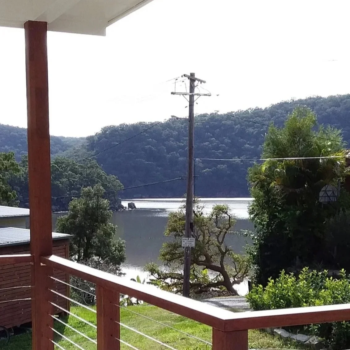 View from a balcony overlooking a lake surrounded by green hills and trees, with power lines and a utility pole in the foreground.
