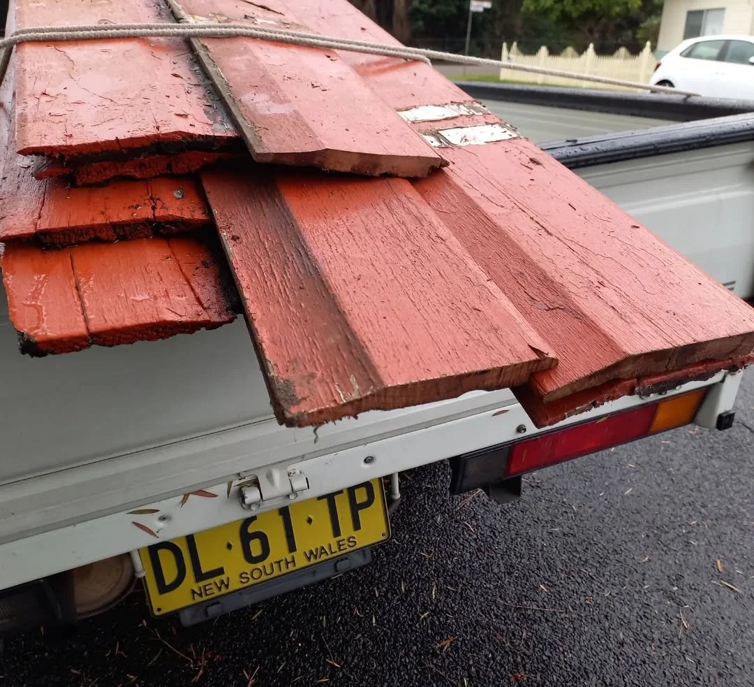 Old weathered red-painted wooden planks on the back of a white pickup truck with a New South Wales license plate. The planks appear to be used for construction or renovation.