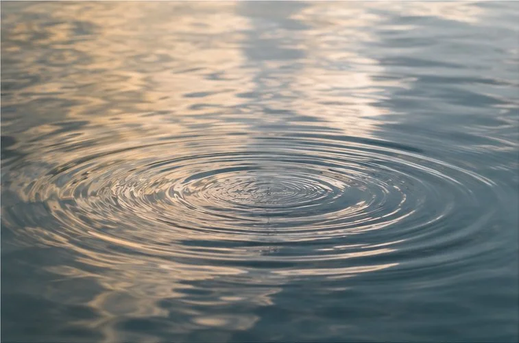 Gentle circular ripples spreading across calm water in soft evening light.