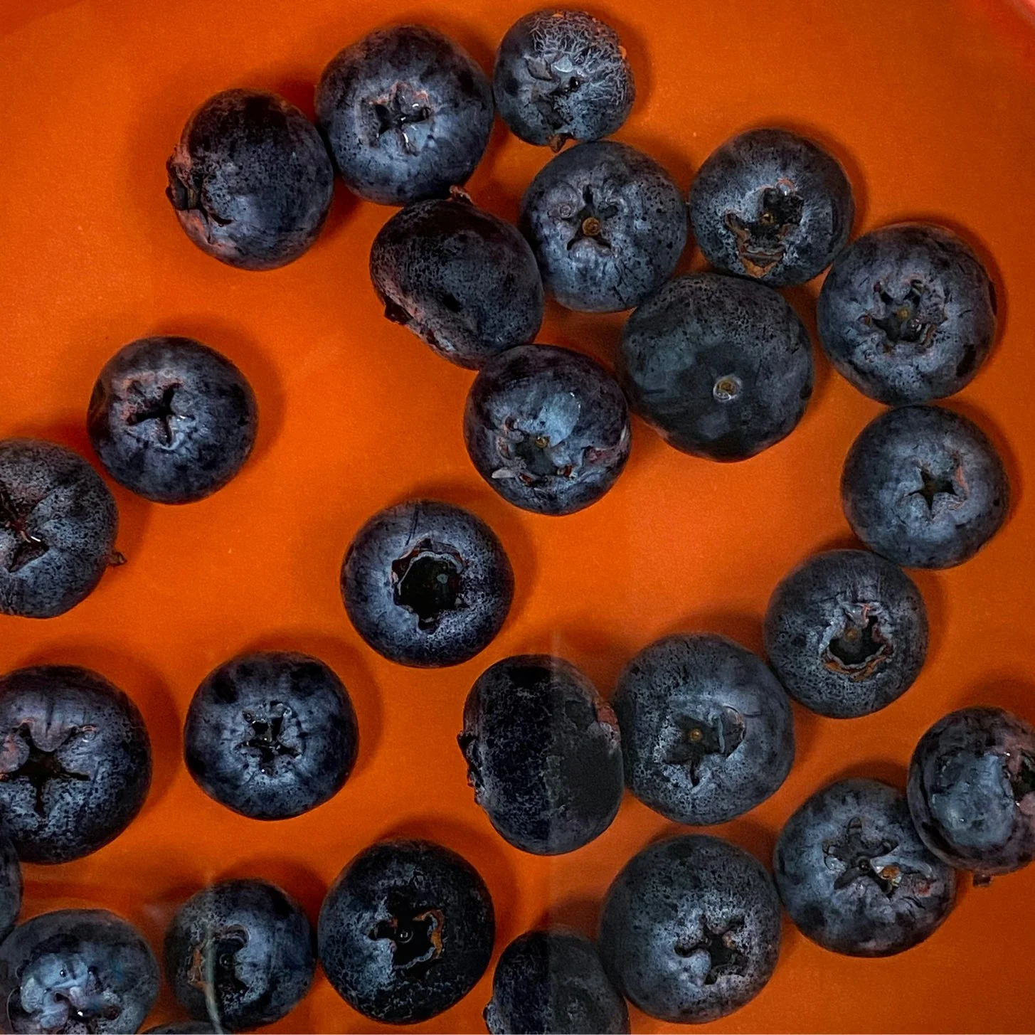 A close-up of fresh blueberries scattered on an orange surface.