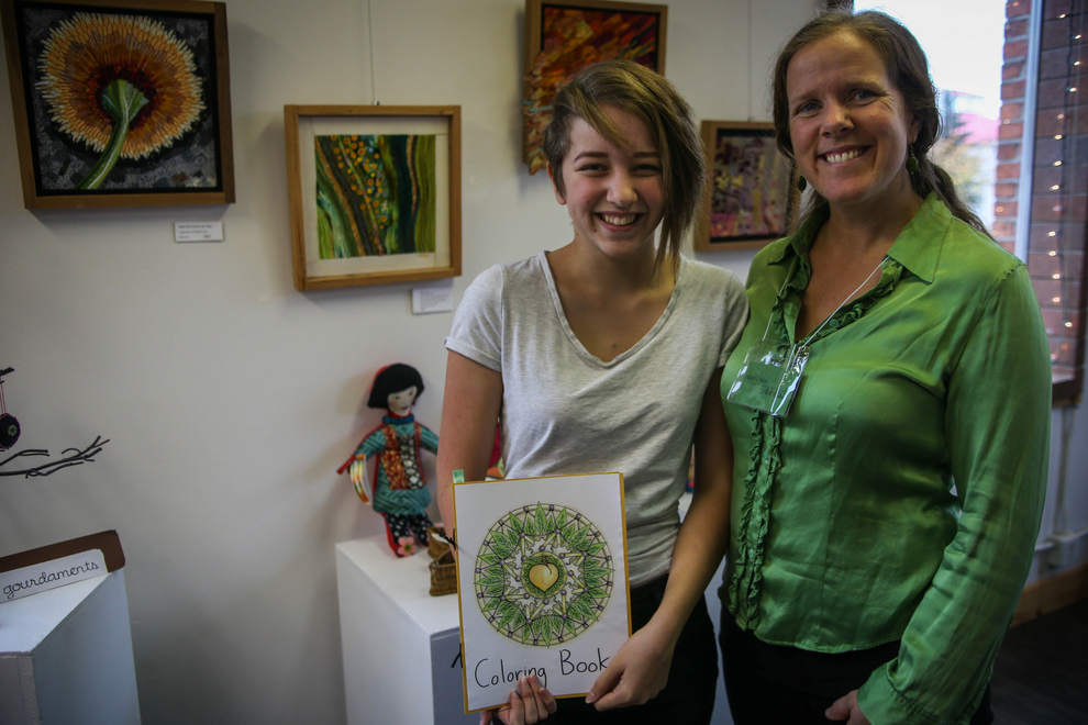 4/10 – Rimona Livie, 14, stands with mom and ArtChic, Mari, at the 11th annual ArtChics Art Sale and Benefit on Saturday at the Lincoln Art Gallery in downtown Eugene. Rimona designed and created coloring books for the sale, while Mari sold her fiber and ceramic artworks. (Mary Jane Schulte/The Register-Guard)