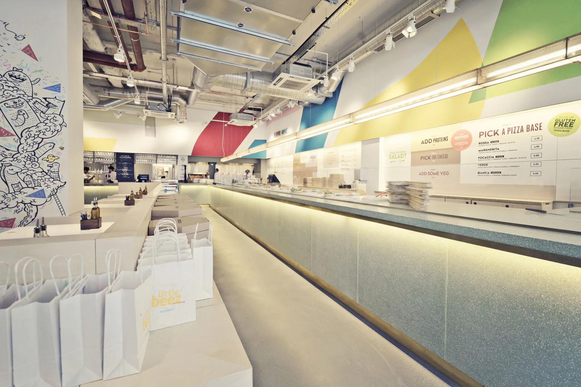 _PIZZABUZZ @ ALPHABETA London, UK Restaurant | 350 sq m Completed 2015 Our proposals for Pizza Buzz introduces a new restaurant typology to London, through which customers create their own ‘bespoke’ pizza with high quality local products, ready to eat in only 120 seconds. This single aspect unit is located between Shoreditch and the City, at the ground floor of the exciting new Alphabeta development. The facade towards the street includes colourful signage across the three window bays, interacting with Worship Street's unique character. Our design intent lies in converting the unit into an extension of the urban environment surrounding it, by echoing cultural references ubiquitous to the immediate context such as street art & materials like concrete, exposed steel and industrial lights. We aim to develop a ‘transient’ environment where customers can choose to stay in a comfortable collection of seating areas or simply use the take-away. Circulation is efficiently planned along the main pizza bar, adapting customer flow to Pizza Buzz's unique service experience. All furniture and lighting was designed and sourced to express the raw qualities of fine materials, delicately assembled. 
