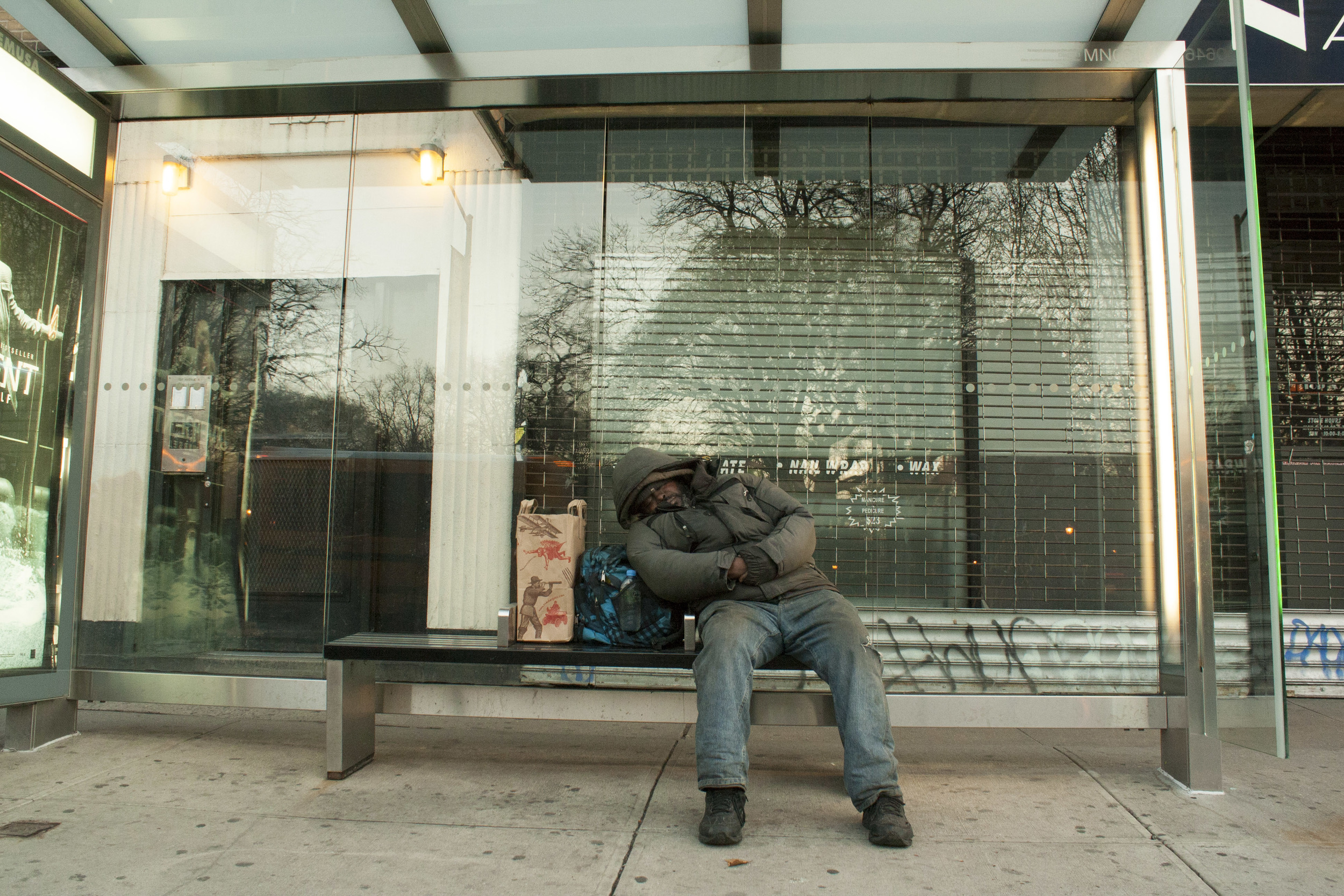A man waits for the bus on Avenue A. 
