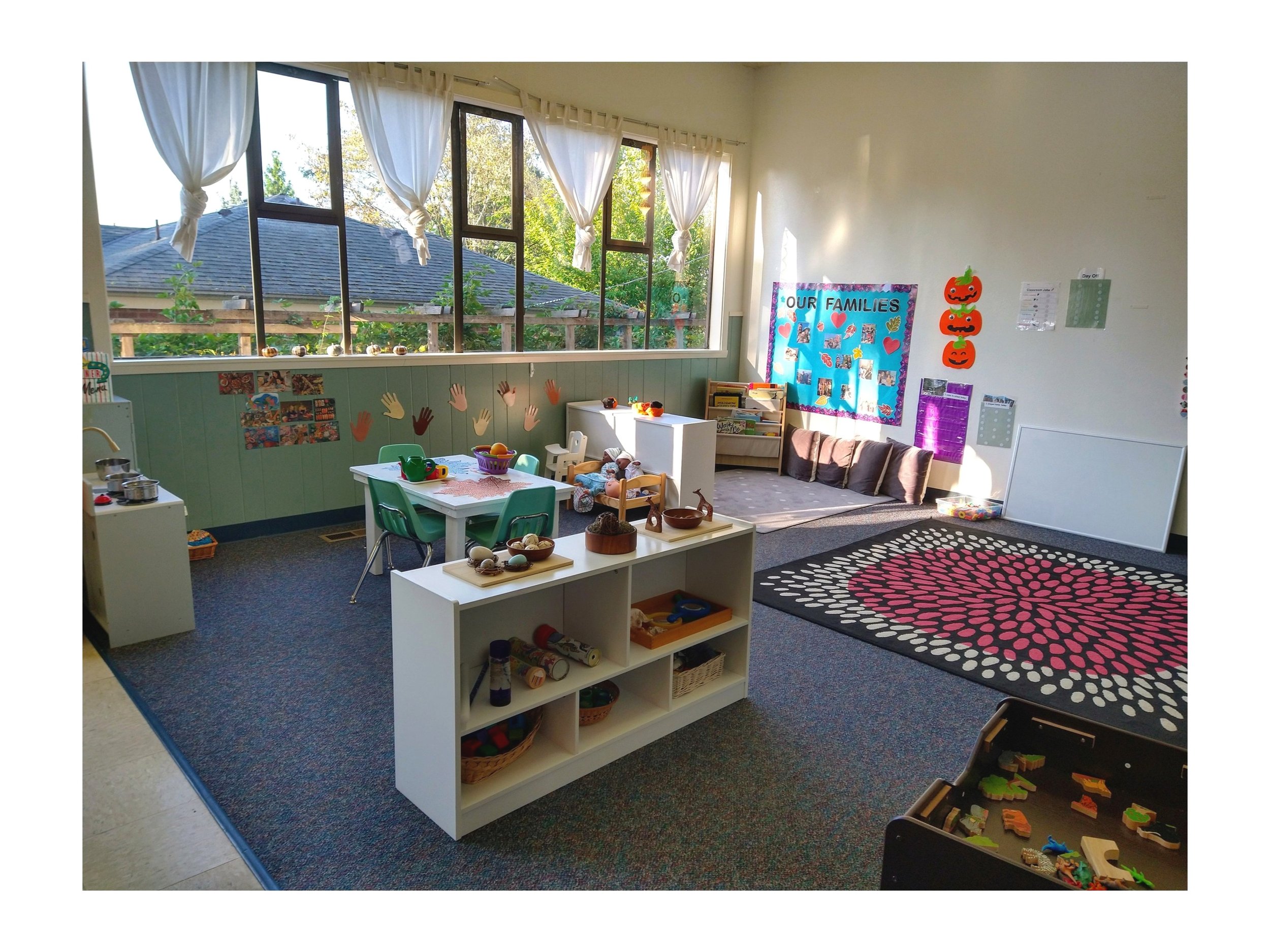  A toddler classroom with large windows and open-ended play materials, including a play kitchen and a reading nook. 