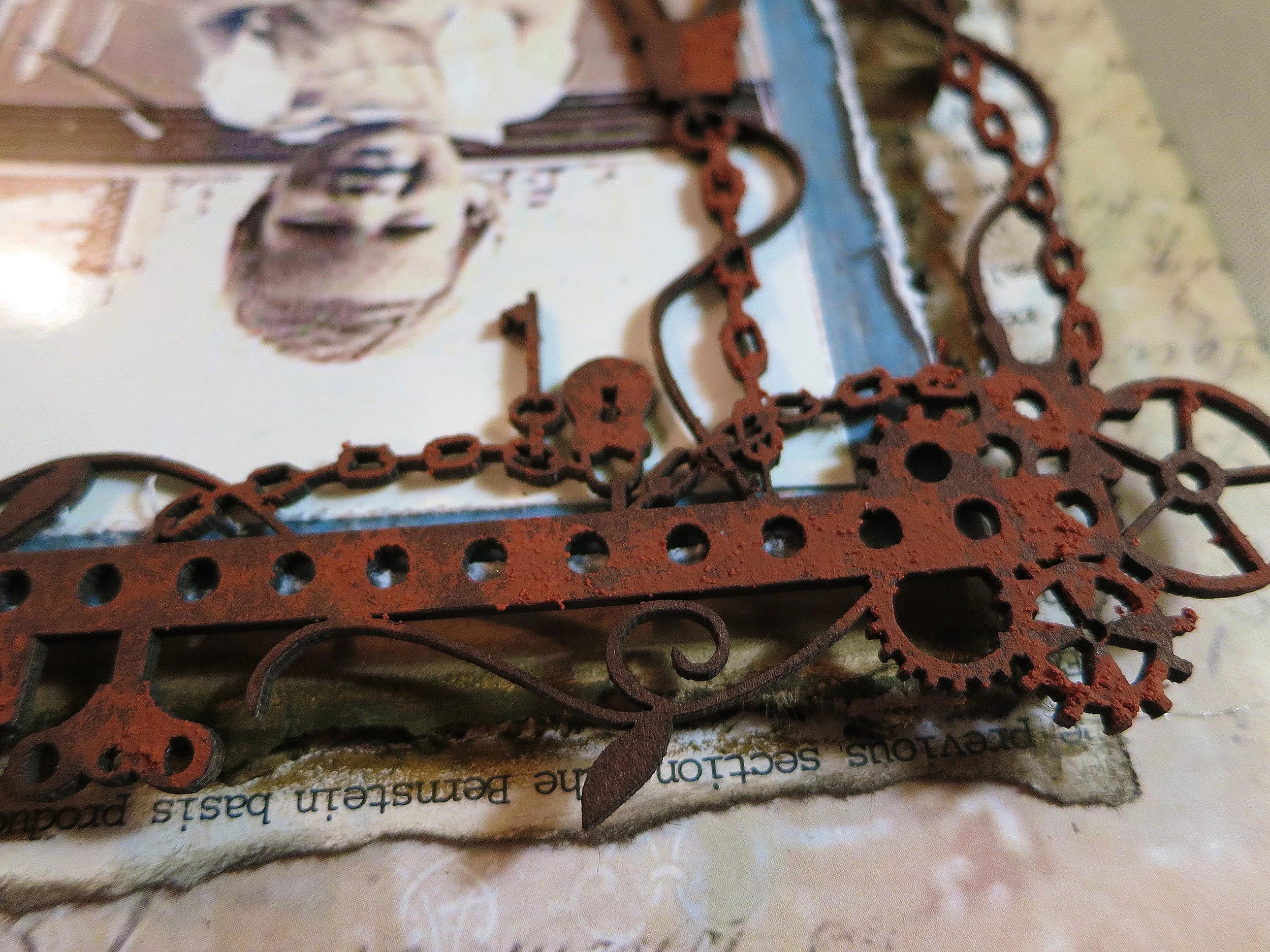I wanted the base of the photo to look like a pile of junk, so I started adding various bits of pieces from the Tim Holtz Ephemera die cuts included in the Main Kit. I used more of the rust pastes on clogs from my stash. 