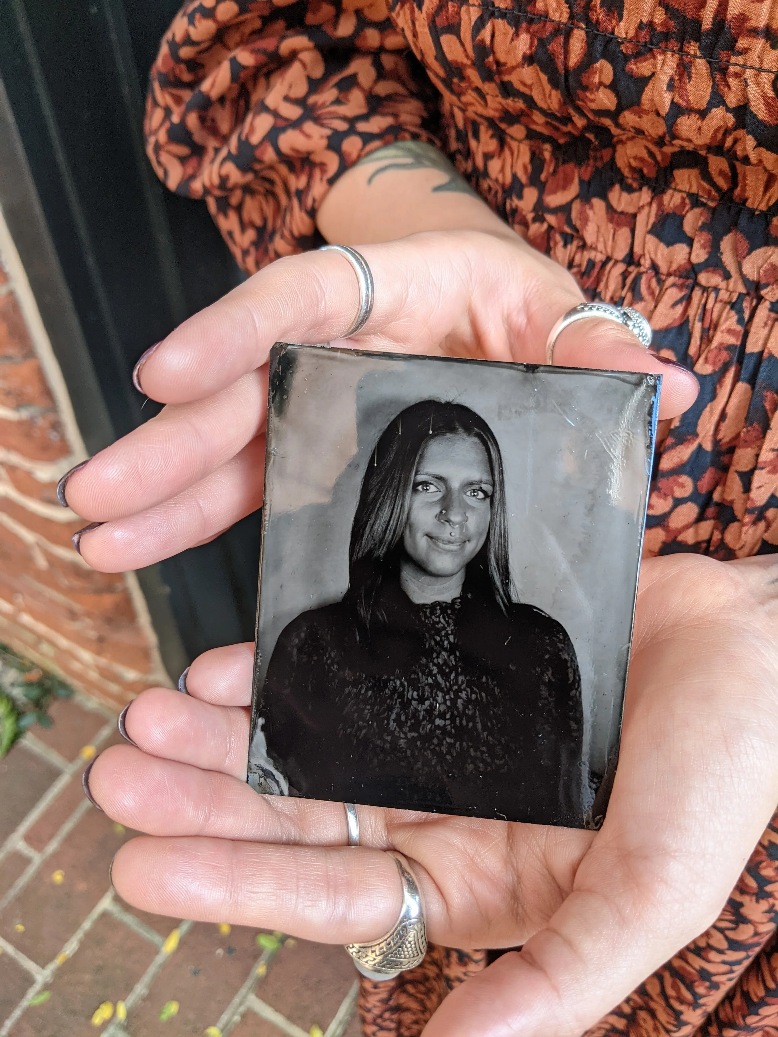 A black and white photograph of a woman with short hair, wearing jewelry and earrings, placed on a red plastic surface near a white wall.