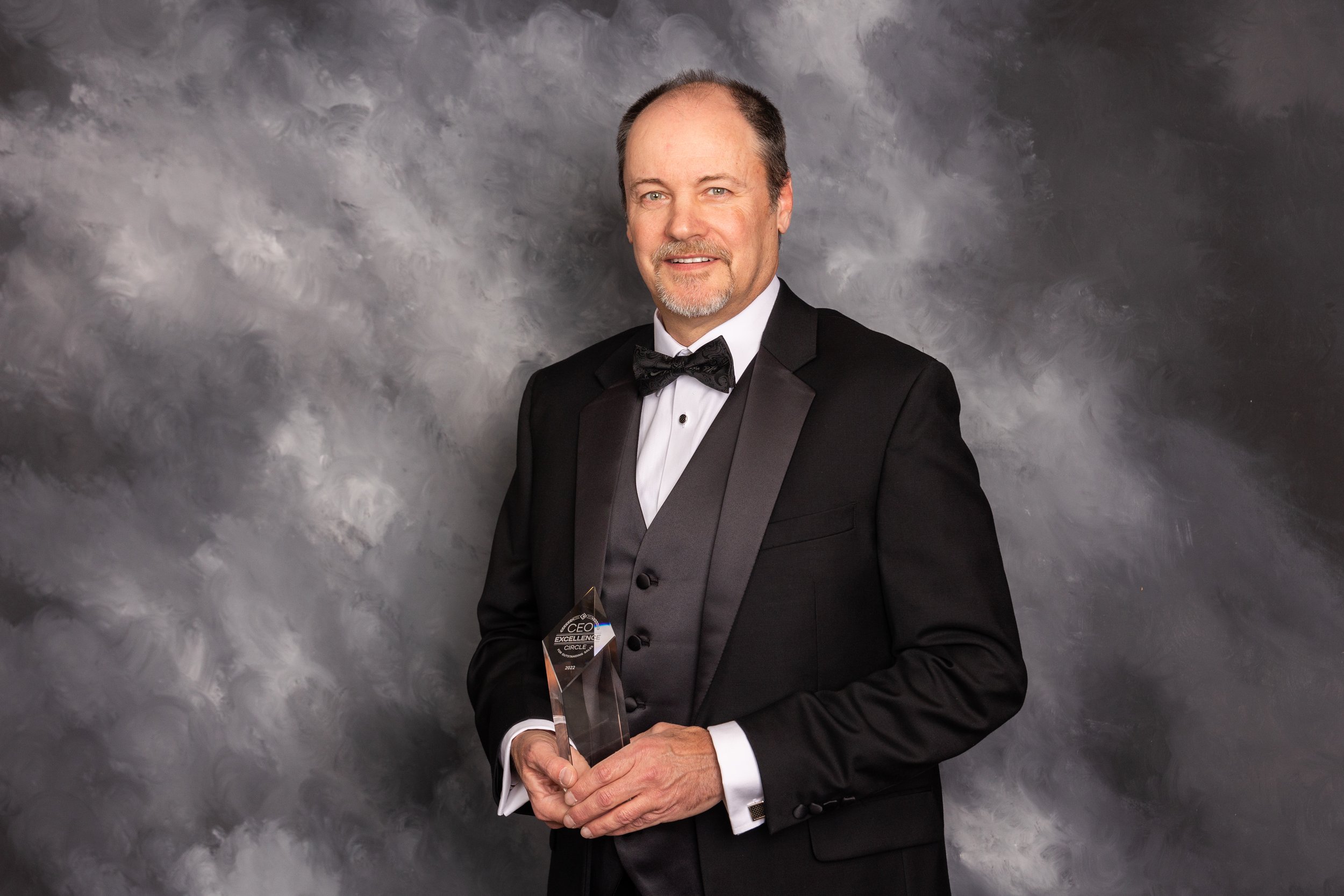 Man in a black tuxedo holding an award at a formal event.