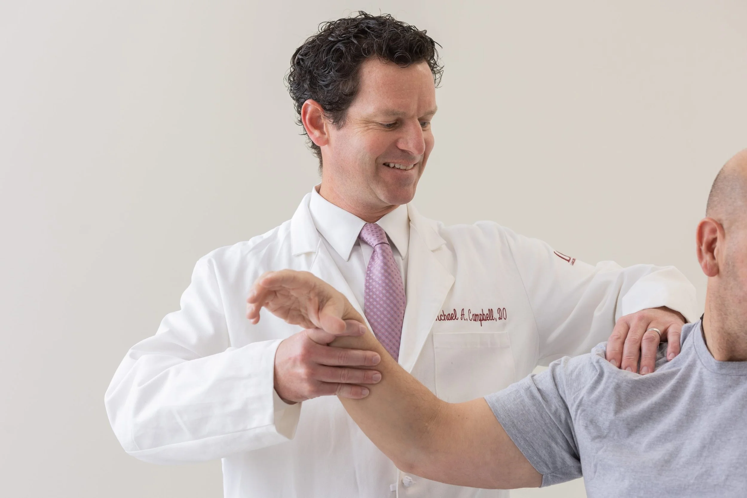 Doctor smiling and examining a patient's arm in a medical setting.
