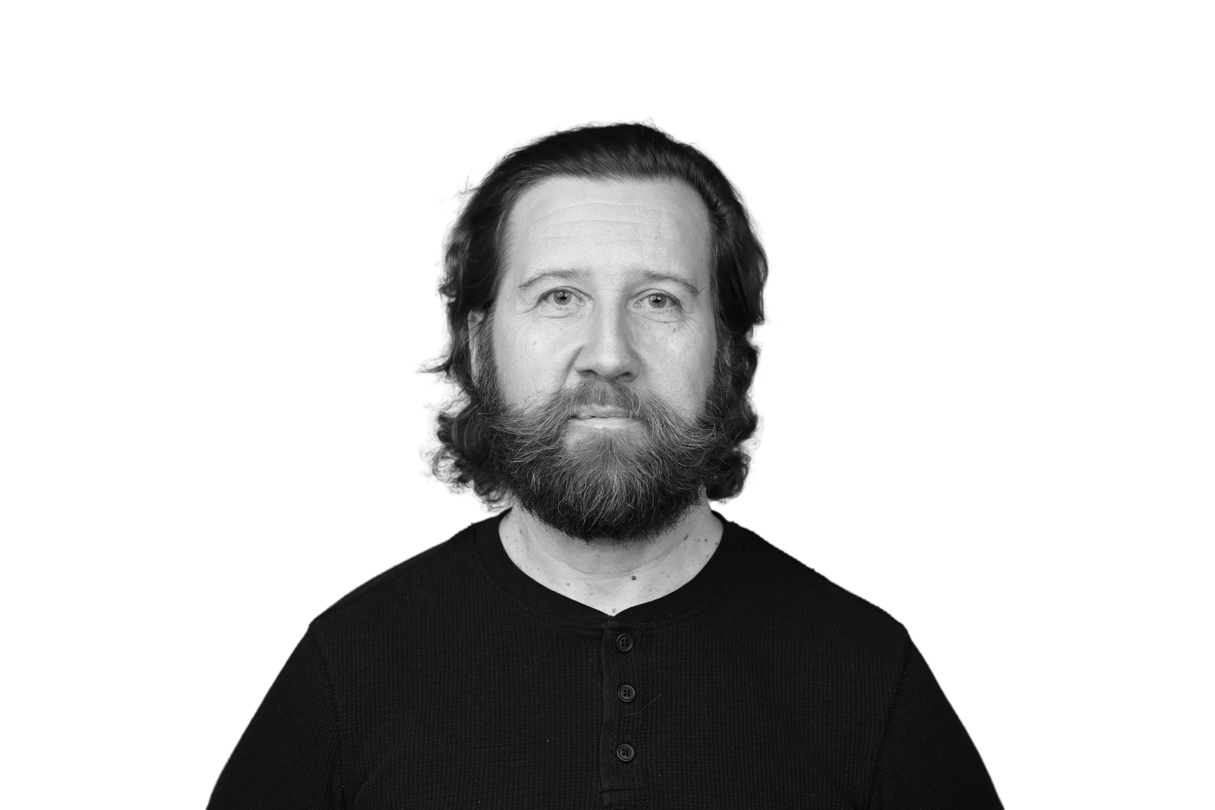 Black and white portrait of a man with a beard and shoulder-length hair, wearing a dark shirt, facing forward with a neutral expression.
