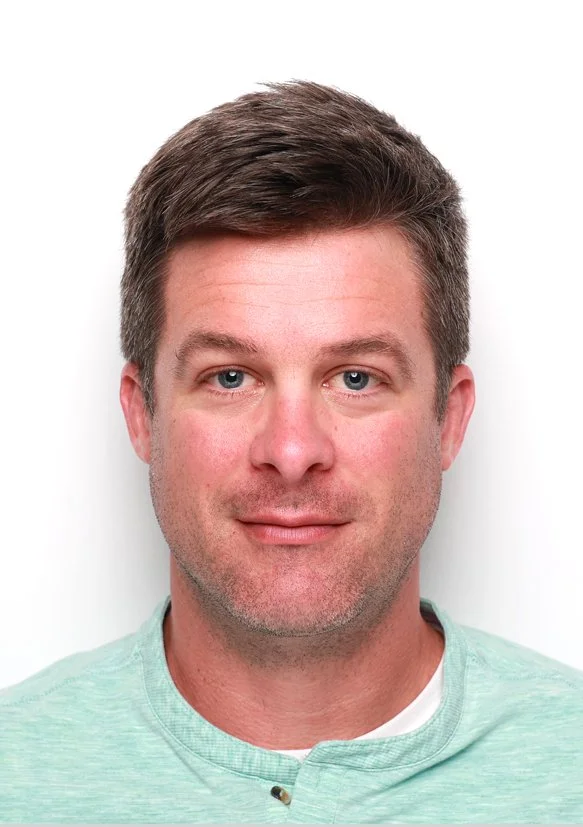 Headshot of a man with short brown hair and blue eyes, wearing a light green shirt.