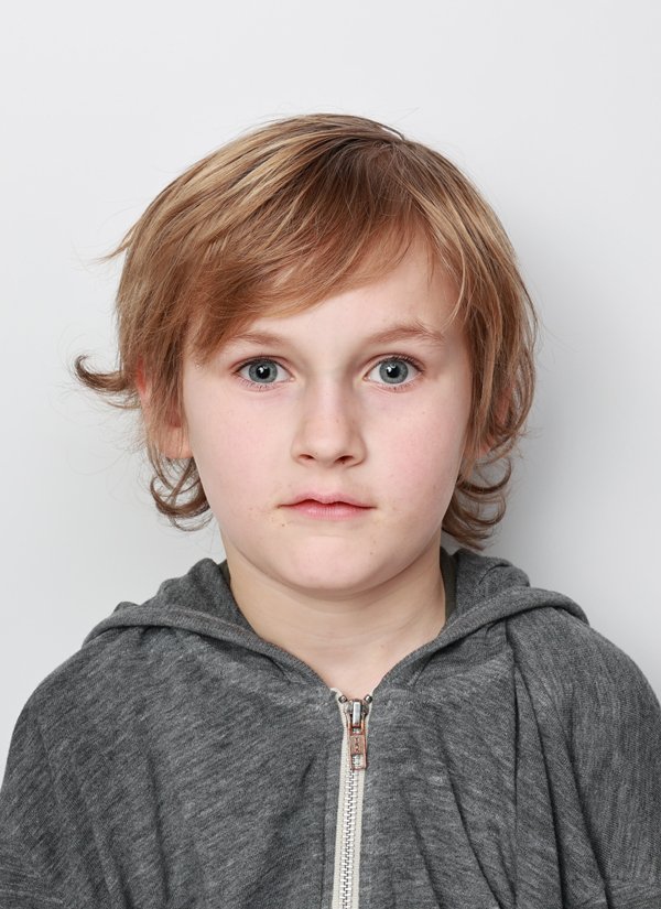 A young boy with blond hair and blue eyes looking directly at the camera, wearing a gray zip-up hoodie, against a plain white background.