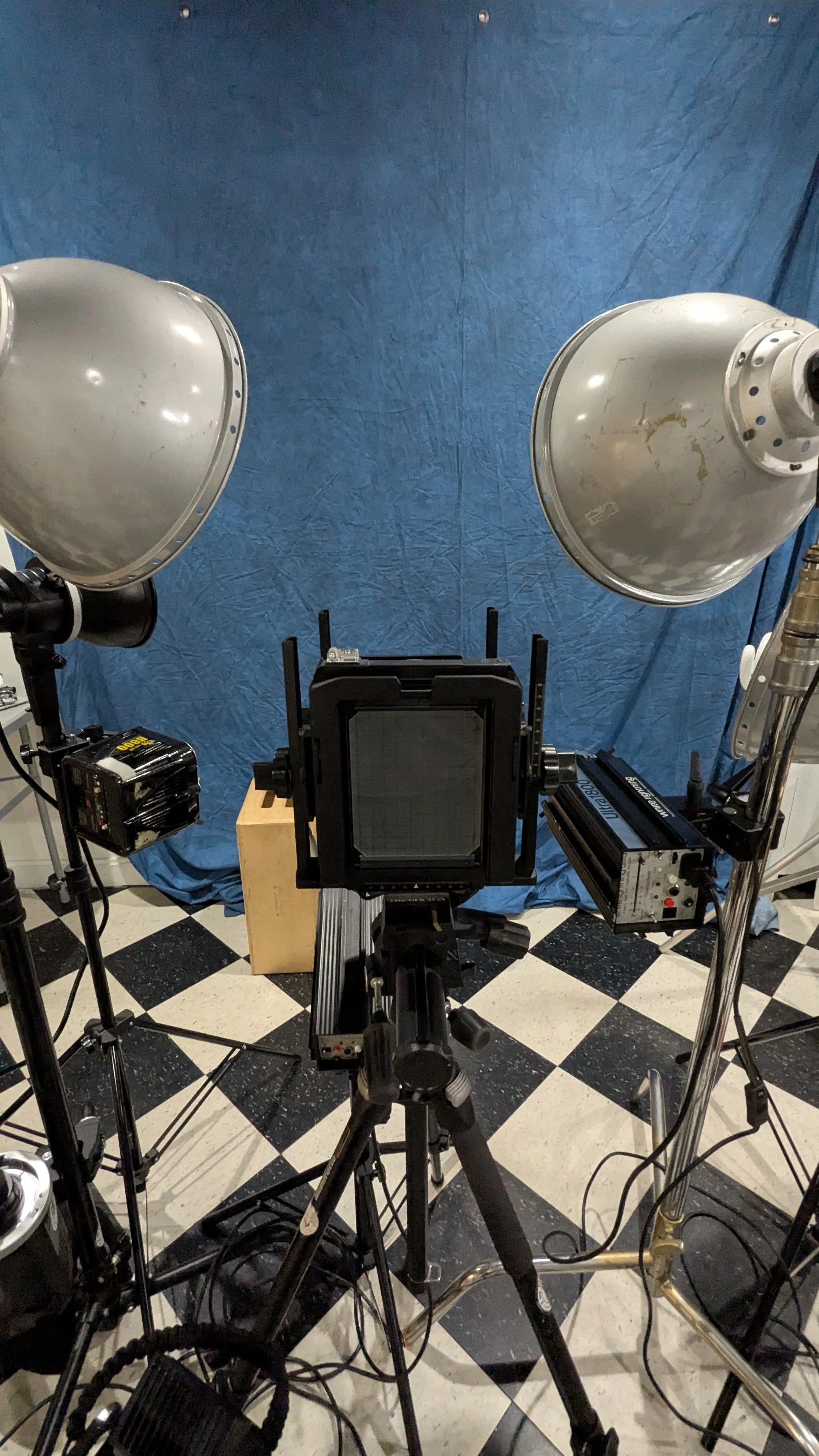 Studio setup with professional cameras, lights, and equipment on a black and white checkered floor with a blue backdrop.