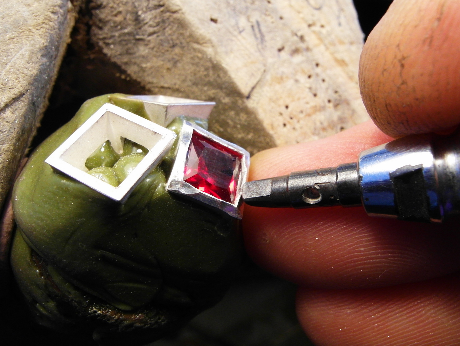  Now hammer down the sides, angling the setting so that you are really looking between the metal and the stone and as even as possible move the metal towards the stone, note the finger underneath the setter is used to ensure no slipping. 