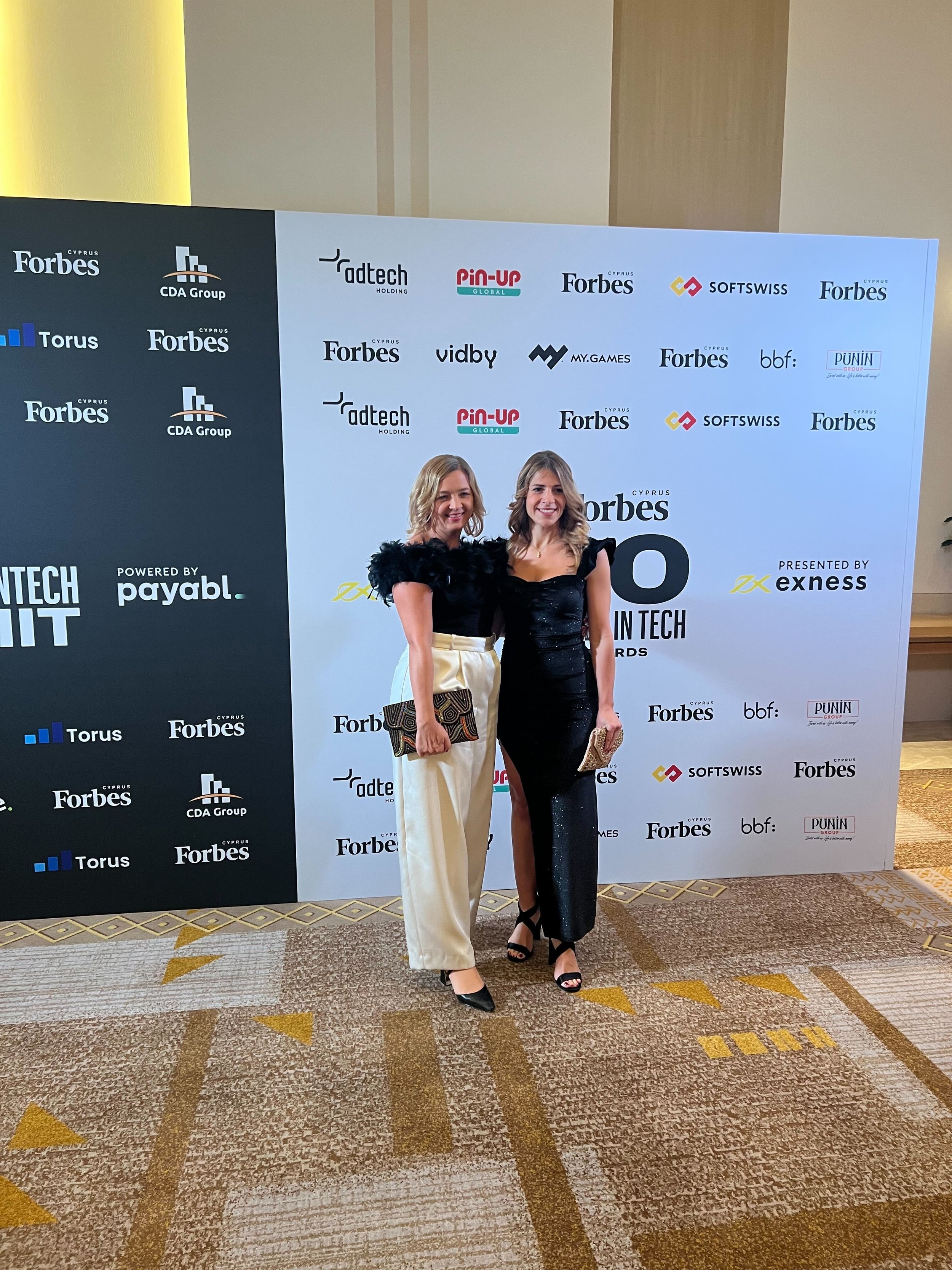  Two women are standing together at the Forbes Cyprus 20 Women in Tech Awards, smiling. 