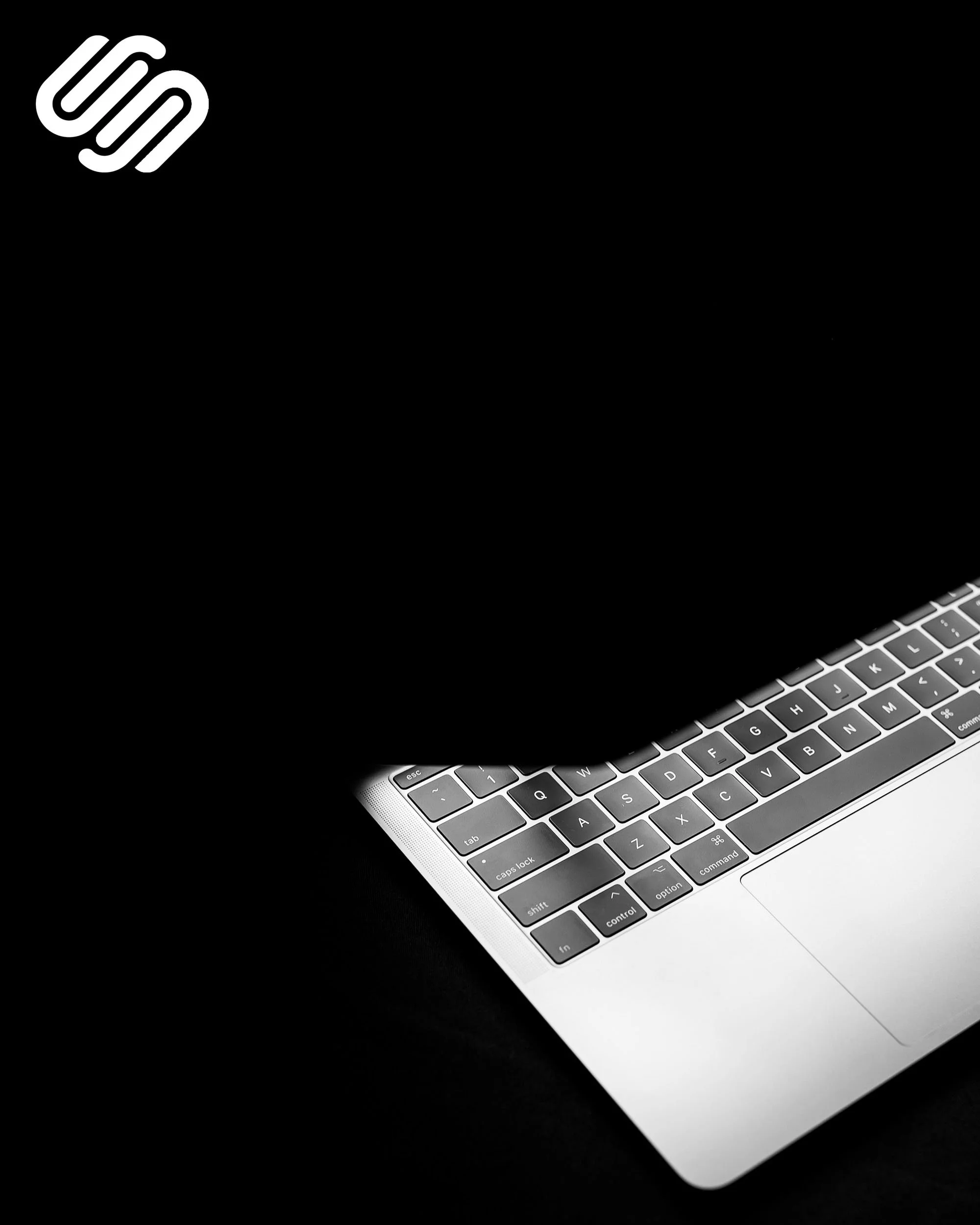 Close-up of a silver Apple MacBook keyboard on a black surface, showing the keys including control, option, command, and various letters.