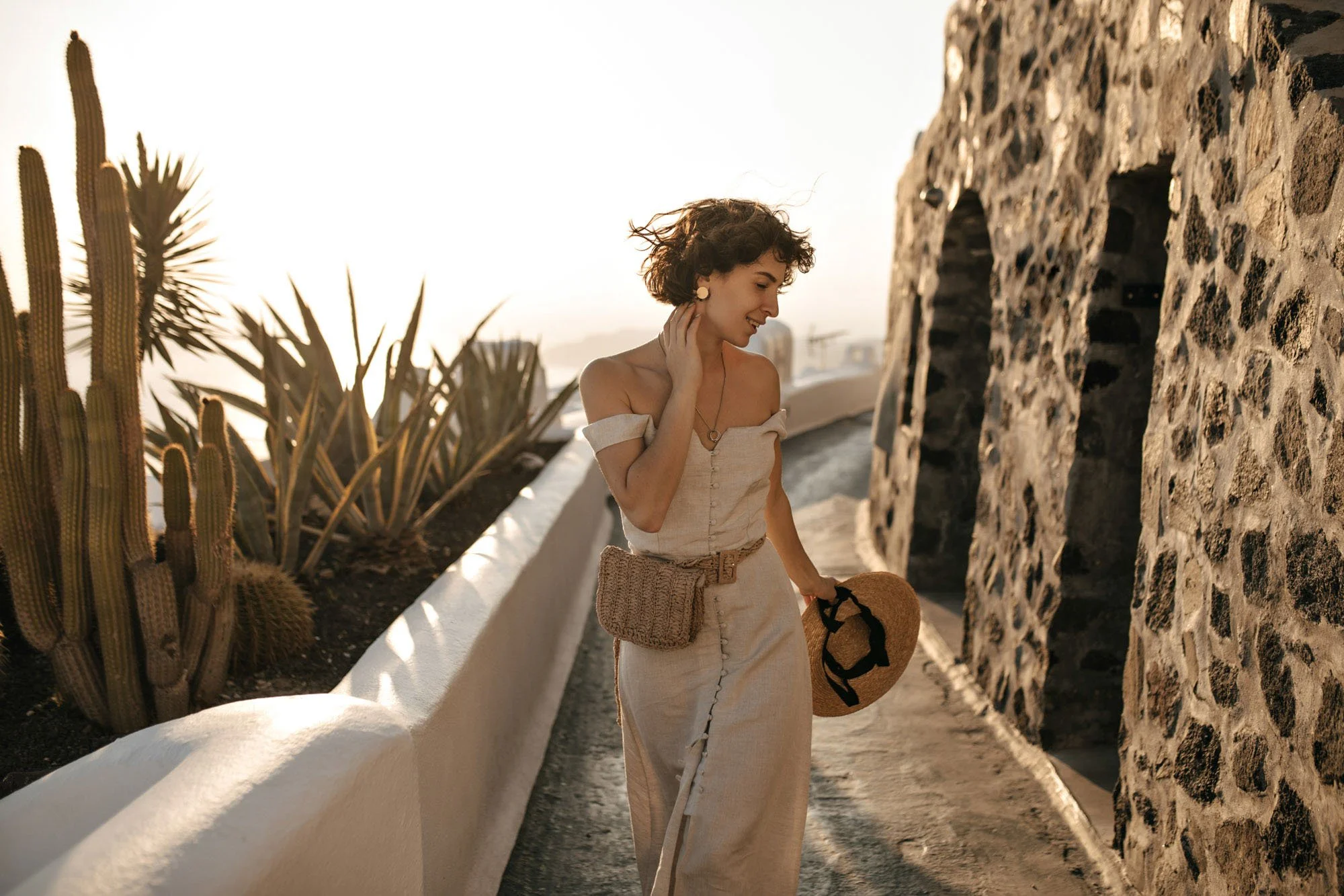 pretty-curly-lady-midi-beige-dress-with-little-straw-bag-holds-boater-brunette-woman-smiles-walks-along-path-old-south-city.jpg