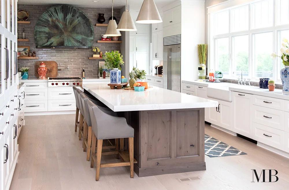 Eclectic yet composed was the guiding design goal for this large and functional kitchen. We created a focal wall behind the range with brick, custom wood shelves and a gorgeous copper range hood. The darker finish on the island brought color cohesion to the space while the natural light made the room a place family and friends will never want to leave.