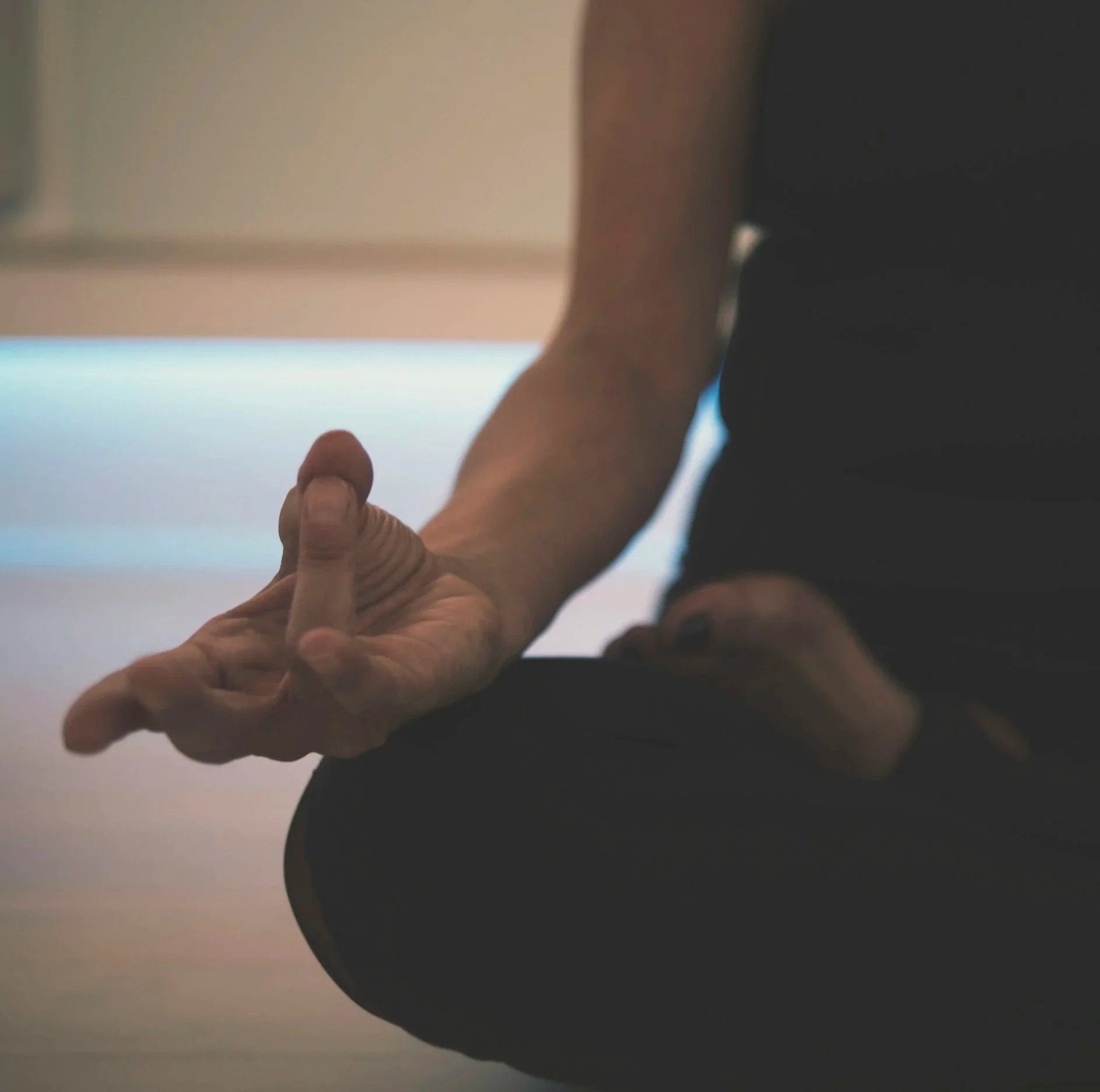A person's hand with a bent index finger while meditate with the background showing part of their arm and some indoors setting.