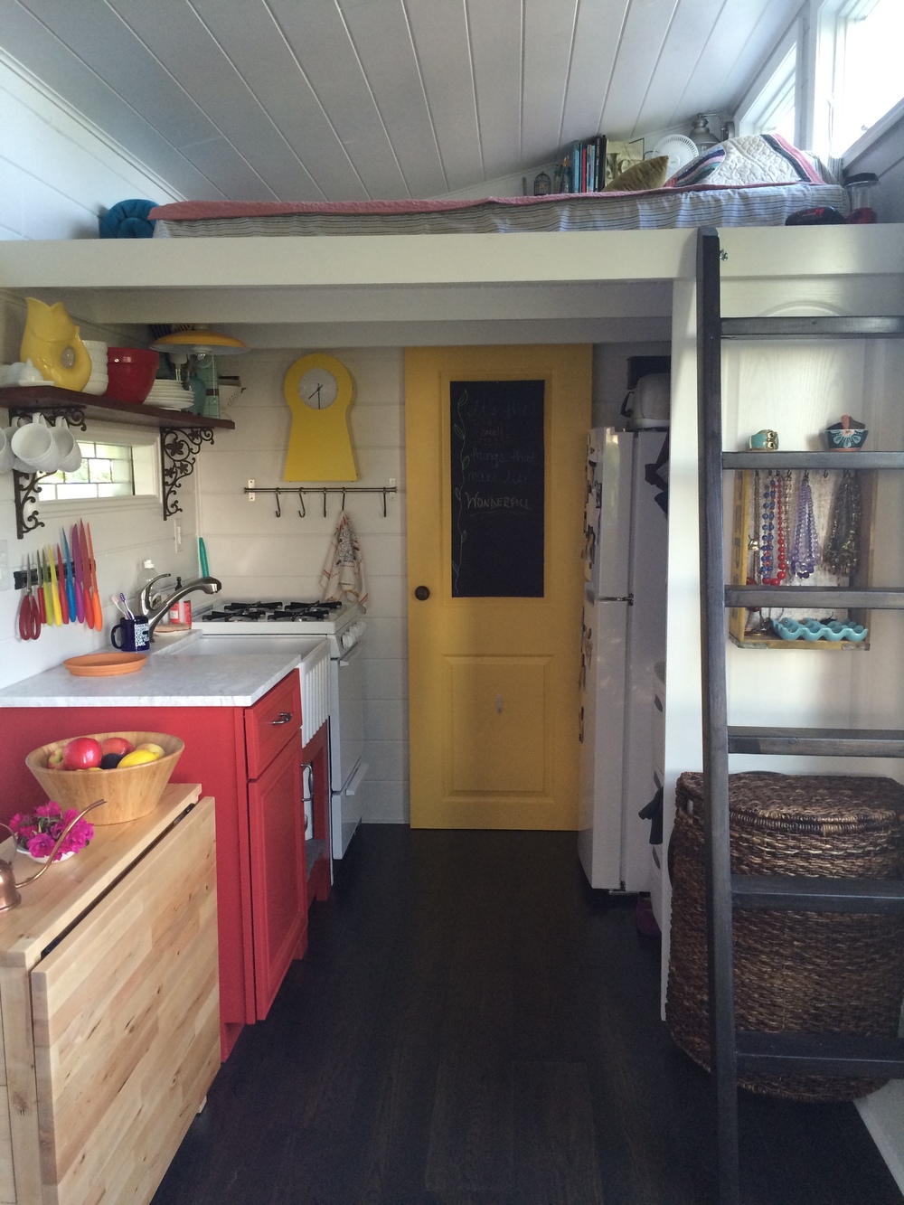  The kitchen area is to the left, refrigerator and closet on the right behind the ladder, sleeping loft on top, and bathroom through the yellow door in the back. 