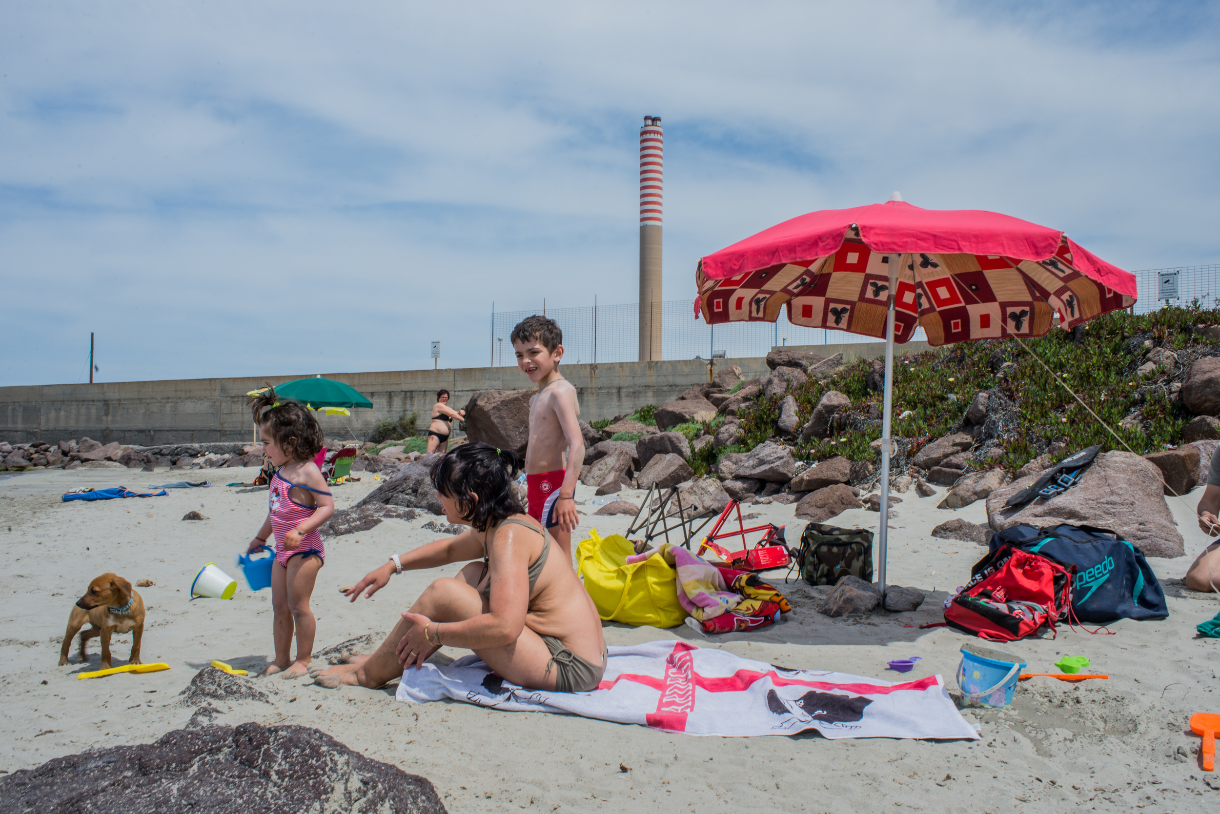  Una famiglia trascorre una domenica estiva in questa piccola spiaggia del porto industriale. In questa insenatura, a ridosso del bacino dei fanghi rossi, vige il divieto di balneazione e di pesca in seguito alla morte di sei persone risucchiate da u